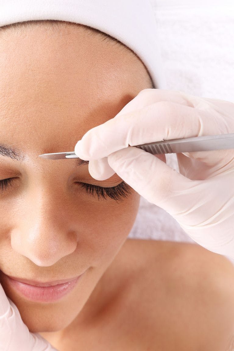 Woman getting dermaplaning treatment, scalpel on brow
