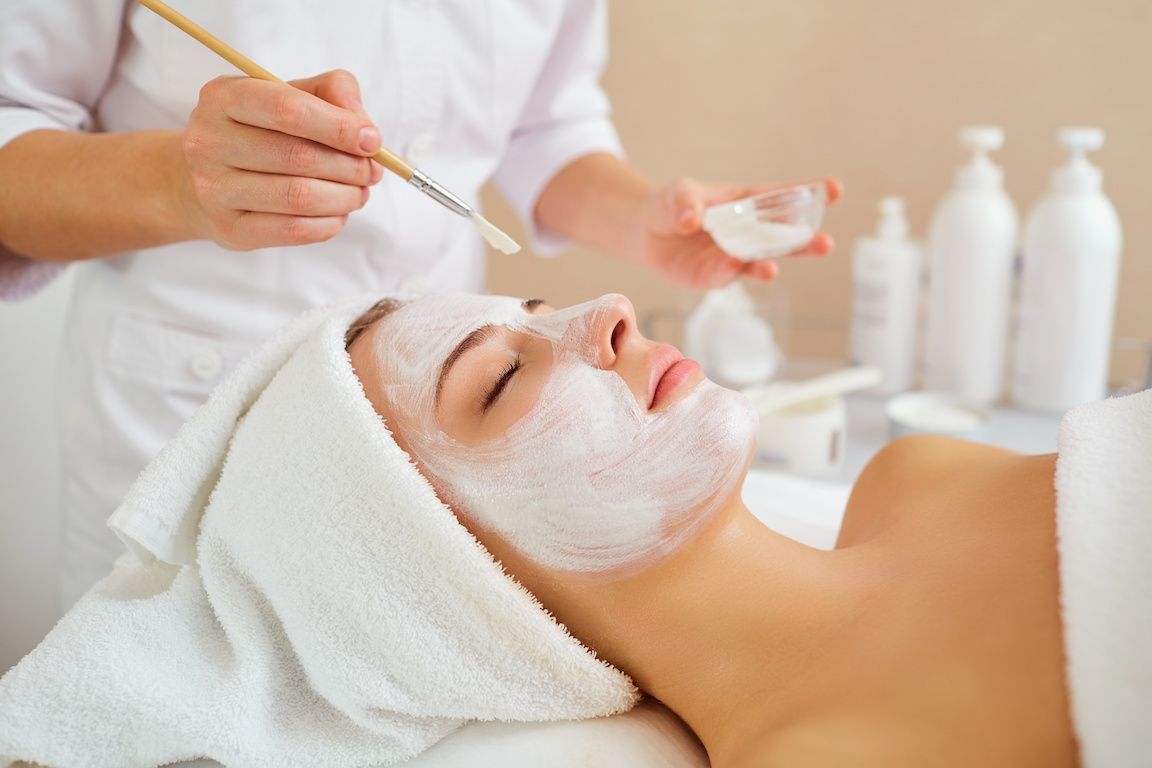 Woman getting chemical peel treatment, brush applying gel/cream, side angle