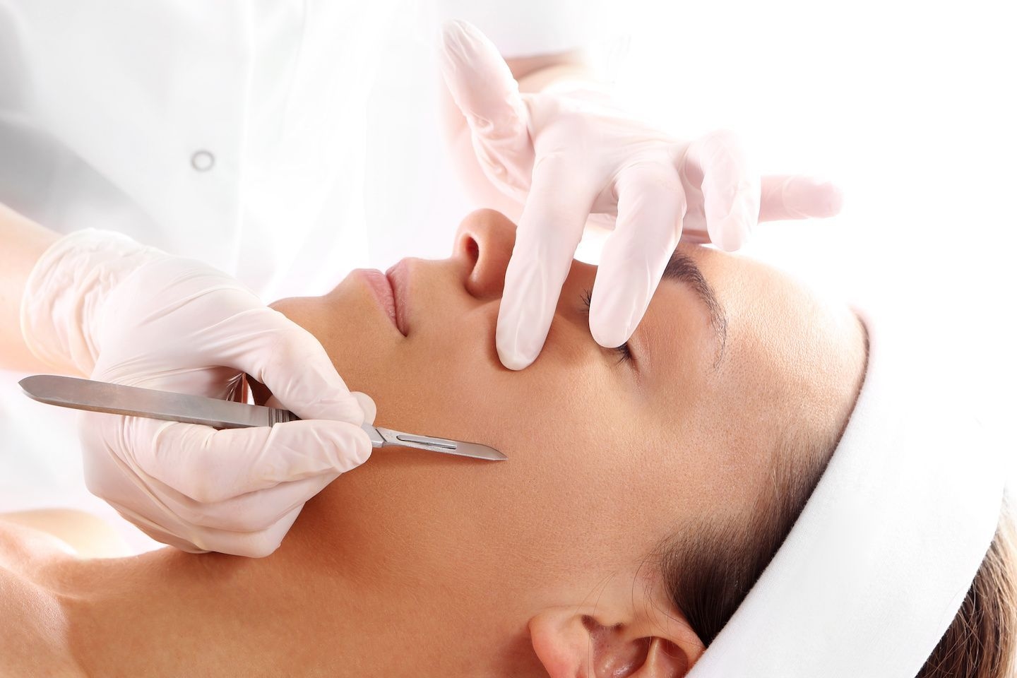 Woman getting dermaplaning treatment, scalpel on cheek