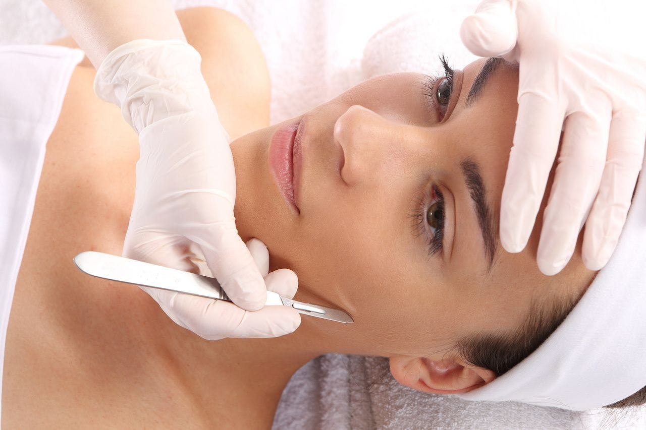 Woman getting dermaplaning treatment, scalpel on cheek